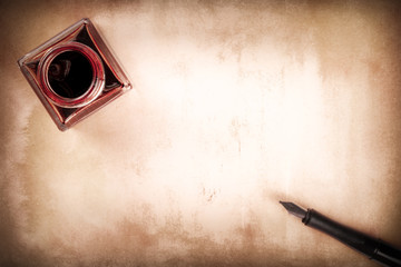 A vintage background with an ink pen and an ink well, shot from above, in sepia tones, old paper with copy space