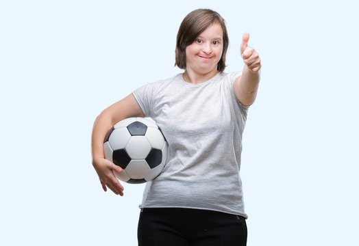 Young adult woman with down syndrome holding soccer football ball over isolated background happy with big smile doing ok sign, thumb up with fingers, excellent sign