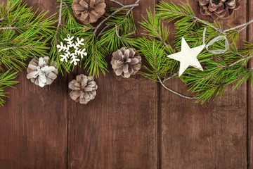 Christmas background with fir tree branches, cones, snow and xmas decorations on a dark wooden texture with copy space