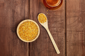 Healthy organic food. Bee pollen, a jar of honey, and a wooden spoon, shot from above on a dark wooden background with a place for text