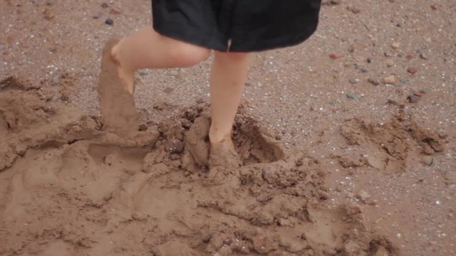 Close up video of the feet of a young boy dancing barefoot in the mud.  He is spinning and wearing a raincoat that is too big and the arms flap as he turns.  Rainy day play.
