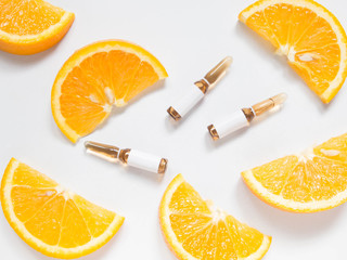 Vitamin C brown ampule for injection with fresh juicy orange fruit slides on white table. High dose vitamin c synthetic for white skin. Beauty product branding mock-up. Healthy lifestyle. Top view.
