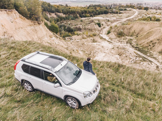 white suv at the top of the hill in autumn overcast weather. man standing near car around wild...