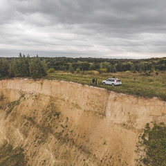 couple standing on cliff in overcast weather near white suv