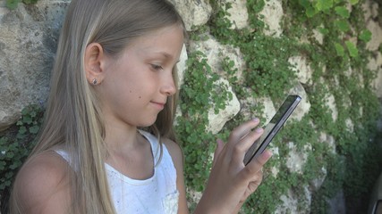 Child Playing Smartphone by Stone Wall in Yard, Little Girl Uses Tablet Outdoor