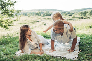 Young Adult Couple with Their Little Daughter Having Fun in the Park Outside the City, Family Weekend Picnic Concept, Three People Enjoying Summer Time