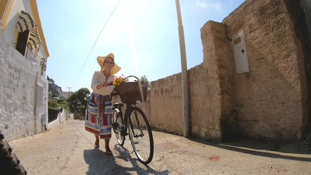 Happy young woman walking with vintage bike through colorful traditional old town in Ponza island Italy. Fashion dress colorful skirt