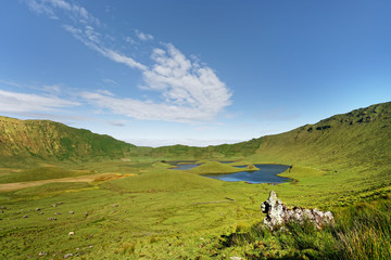 Obraz premium The crater of the volcano of the Azorean island of Corvo has huge dimensions, lakes in the crater center, striking cloud formation, rocks in the foreground - Location: Portugal, Azores, Corvo Island