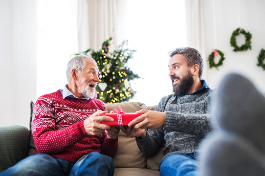 A senior father and adult son with a present sitting on a sofa at Christmas time.