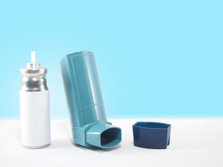 Blue asthma inhaler and blank label cartridge on white table w/ blue gradient background. Pharmaceutical product for treat or prevent asthma attack. Health medical concept. Copy space.