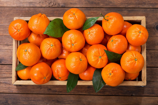 Fresh mandarin oranges fruit or tangerines with leaves in wooden box
