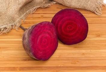 Uncooked red beetroot cut in half on bamboo cutting board