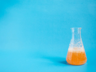 Chemical laboratory flask with orange solution and bubble on blue background with copy space. Concept of science, chemistry, analysis, toxicology, research and development concept. Minimal style.