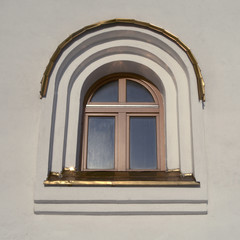 Obraz premium A window with a wooden frame with an arched top, covered with copper sheets. An element of architecture of an Orthodox church.