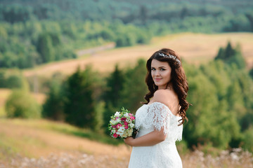 Beautiful brunette girl with a bouquet of flowers. Young woman with long curly hair in a white lace dress. Summer female portrait