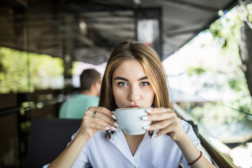 Young pretty woman in a cafe drinking coffee on terrace