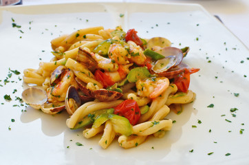Shrimps squids and other seafood in salad with pasta on a white ceramic plate in an Italian restaurant