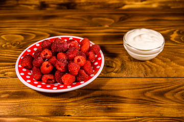 Ceramic plate with ripe raspberries and sour cream on wooden table