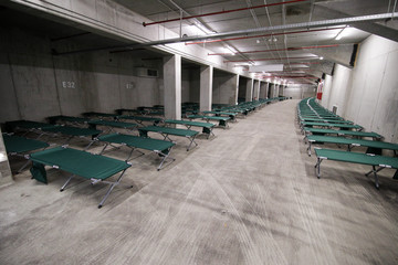 Camp folding cots are being set up in the underground parking of a stadium