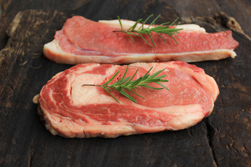 Raw beef steak with rosemary on wooden dark background, food meat or barbecue