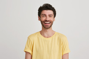 Portrait of smiling happy attractive young man with dark brown hair and beard wears yellow tshirt, isolated over white background