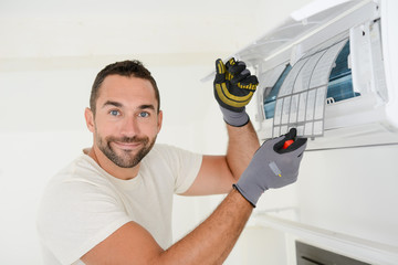 handsome young man electrician cleaning air filter on an indoor unit of air conditioning in a client house