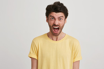 Young brown hair man with beard looks bawling and yelling, wears yellow classic tshirt, isolated over white background