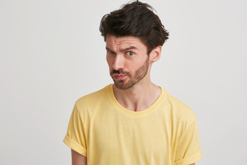 Obraz premium Dark hair young man with beard wearing yellow tshirt looks suspicious and showing defiance,isolated over white background