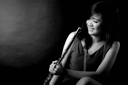 Fashion portrait in studio of beautiful young woman feeling happy with her flute against dark background in studio