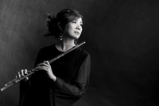 Fashion portrait in studio of beautiful young woman feeling happy with her flute against dark background in studio