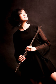 Fashion portrait in studio of beautiful young woman feeling happy with her flute against dark background in studio