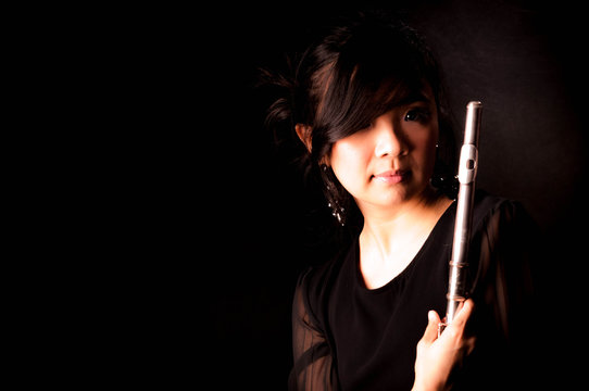 Fashion portrait in studio of beautiful young woman feeling happy with her flute against dark background in studio