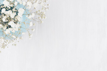 Spring bouquet of white small fluffy flowers in blue smooth circle ceramic vase top view on soft white wood background.