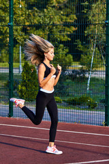 Obraz premium Sport girl. The girl is doing fitness exercises. Beautiful young sports woman doing exercises. A girl is training on a sports field. Young beautiful girl in sports uniform posing on sports field.