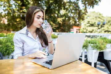 Smiling business woman portrait outdoors with laptop and glass of water.
