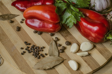 Bell red pepper with celery leaves, bay leaves, garlic and allspice lie on a wooden striped cutting board
 
