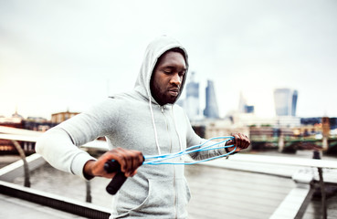Young active black sportsman with skipping rope in a city, wearing hoodie.