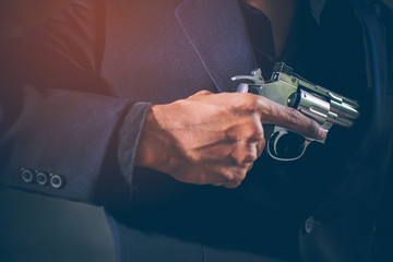 A close-up of a hand, the young man, wearing a black suit, pulling a Revolver out of the Holster under jackets on a dark background. He holding gun in hand. Secret agent, mafia, bodyguard concept.