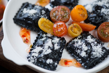 Close-up of black italian ravioli with cherry tomatoes and grated parmesan cheese, selective focus