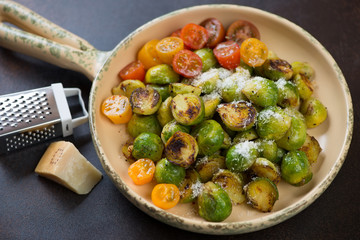 Roasted brussels sprouts with cherry tomatoes and grated parmesan in a serving pan, studio shot