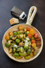 Serving pan with fried brussels sprouts, tomatoes and cheese, studio shot on a brown metal background