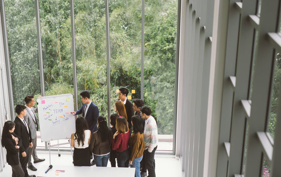 Businessman presenting at whiteboard Gruop of business people standing around white board during meeting in office - Powered by Adobe