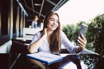 Young pretty woman make notes in notebook while have video call conversation or blogger translation in outdoors cafe