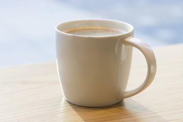 White coffee mug on the table by the window, close-up
