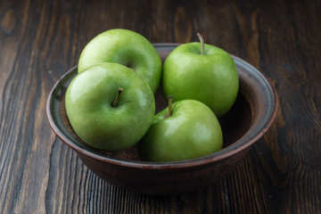 Green apples in a clay Bowl. On a rustic background.