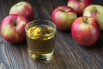 Glass of apple juice with red apples on wooden table, closeup