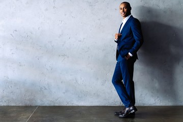 Full length smiling business man in black suit looking at camera and standing isolated on gray background.