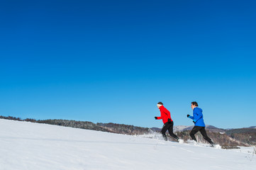 A side view of senior couple jogging in snowy winter nature. Copy space.