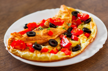omelette with tomato, pepper and olive in white plate on wooden table background