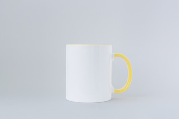 A white mug, with a yellow handle on a light background. 